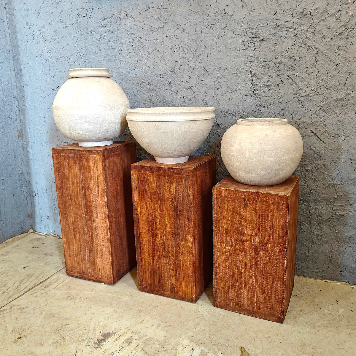 Minimalist wooden display risers holding handcrafted white clay vases in a multi-level arrangement.
