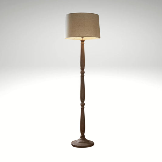 raditional wooden floor lamp featuring a distressed brown turned pillar stem and a tan drum lampshade.