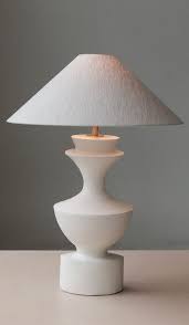 Sculptural ceramic table lamp in white with a wide cone shade resting on a flat surface.