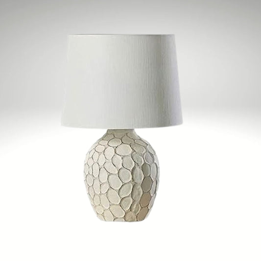 Cream-colored bedside lamp with a sculptural, stone-textured oval base and a clean white fabric lampshade.