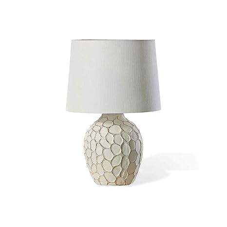 Cream-colored bedside lamp with a sculptural, stone-textured oval base and a clean white fabric lampshade.