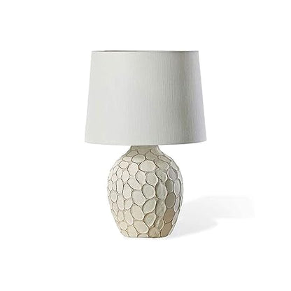 Cream-colored bedside lamp with a sculptural, stone-textured oval base and a clean white fabric lampshade.