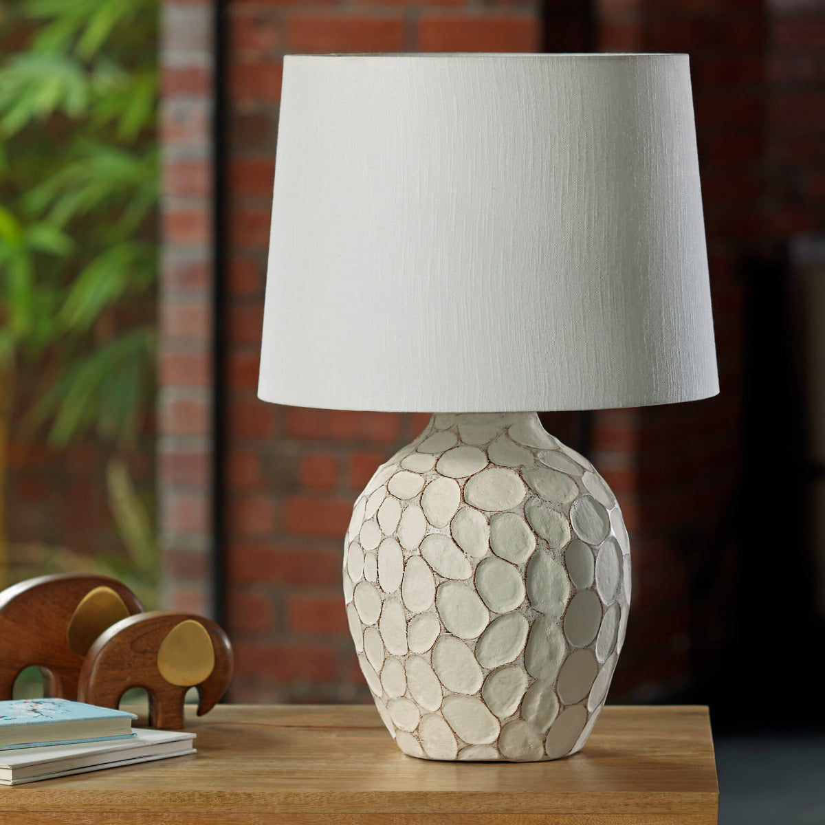 Cream-colored bedside lamp with a sculptural, stone-textured oval base and a clean white fabric lampshade.
