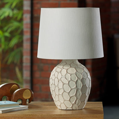 Cream-colored bedside lamp with a sculptural, stone-textured oval base and a clean white fabric lampshade.