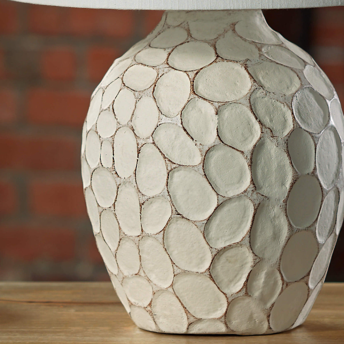 Cream-colored bedside lamp with a sculptural, stone-textured oval base and a clean white fabric lampshade.