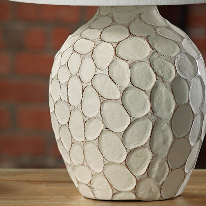 Cream-colored bedside lamp with a sculptural, stone-textured oval base and a clean white fabric lampshade.
