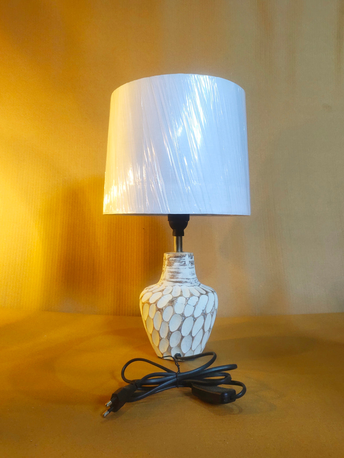 Cream-colored bedside lamp with a sculptural, stone-textured oval base and a clean white fabric lampshade.