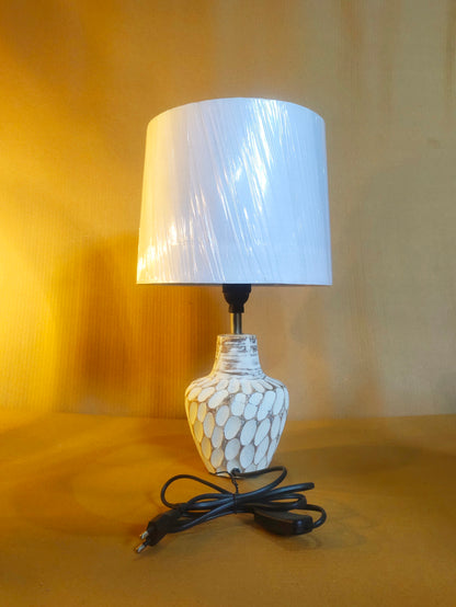 Cream-colored bedside lamp with a sculptural, stone-textured oval base and a clean white fabric lampshade.
