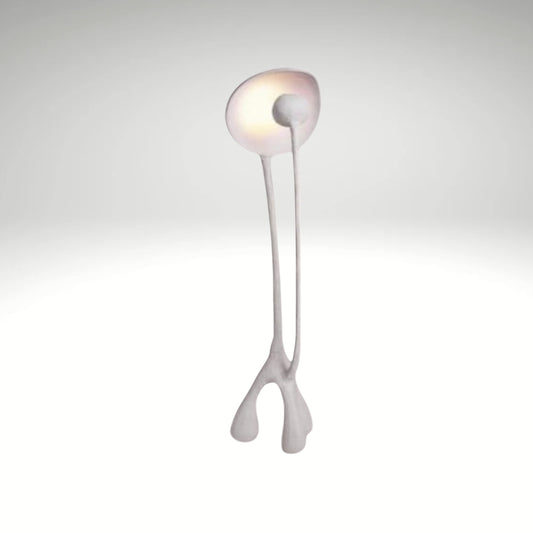 A modern white sculptural floor lamp with a slender twin-stem body and a warm, diffused oval reflector light at the top.
