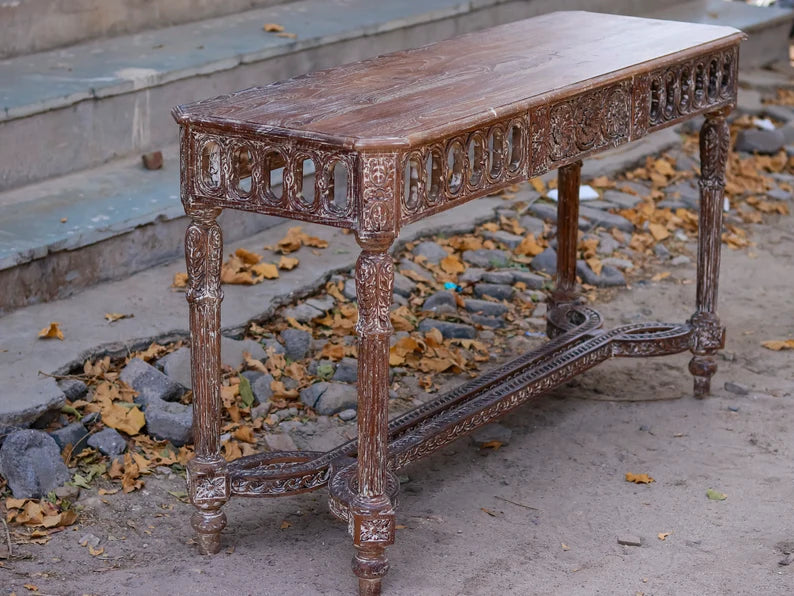Rustic hand-carved solid wood console table with a weathered finish, standing outdoors on a stone and dirt path.