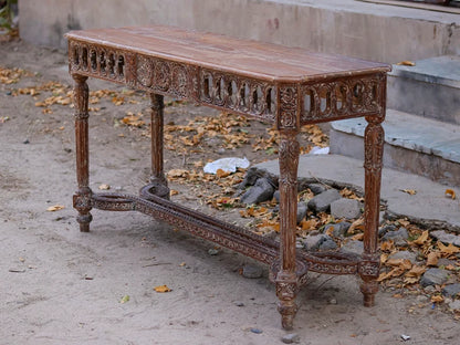 Rustic hand-carved solid wood console table with a weathered finish, standing outdoors on a stone and dirt path.