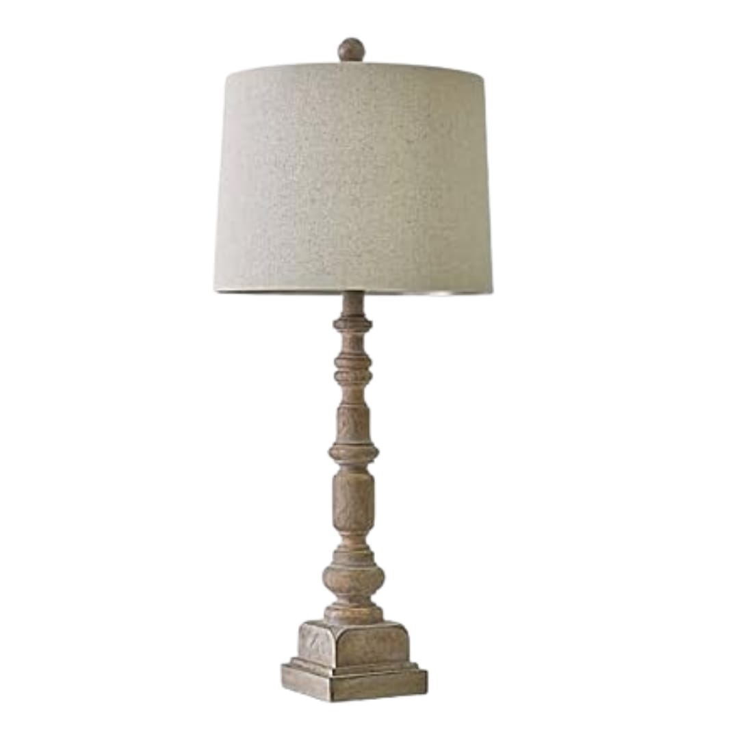 A traditional table lamp featuring a distressed, turned-wood candlestick base and a neutral beige fabric drum shade