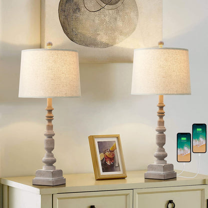 A traditional table lamp featuring a distressed, turned-wood candlestick base and a neutral beige fabric drum shade